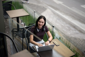 Fototapeta premium Smiling young woman typing on laptop at outdoor cafe