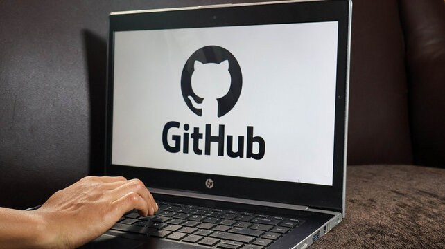 A person interacting with a laptop displaying the github logo on the screen in a dark room with a brown couch
