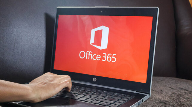 A person using a laptop with the microsoft office 365 logo on the screen on a brown surface