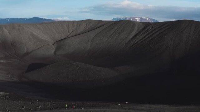 Aerial drone footage captures tiny hikers on the edge of a vast, desolate volcanic crater under