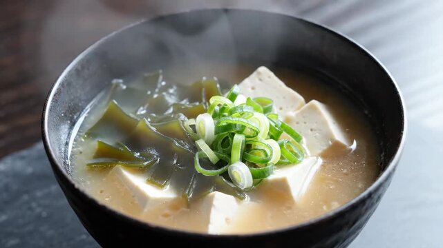 Steaming hot Japanese miso soup with tofu cubes, wakame seaweed, and fresh green onions in a bowl.