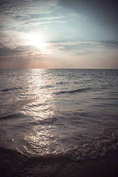 Scenic seascape view of bright sun setting over the ocean with golden reflection on water surface and sand beach