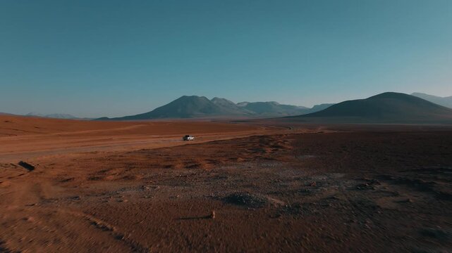 Aerial view of a 4x4 driving across the vast wilderness of Sud L&iacute;pez, Bolivia. Volcanic mountains and high-altitude deserts stretch to the horizon.