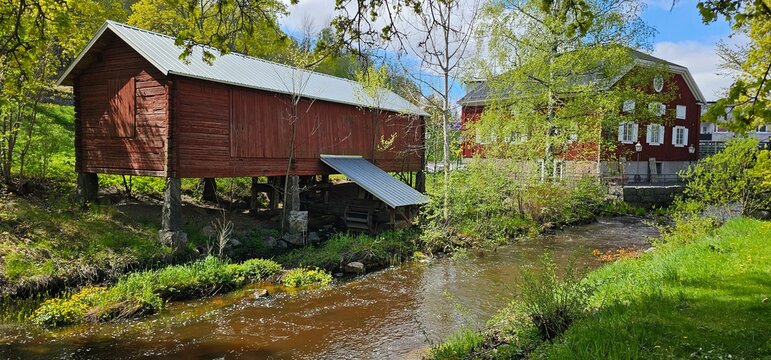 A historical Falu-red mill building resting on a stone foundation and standing next to a flowing stream. S&ouml;derhamn Sweden. historisk kvarn