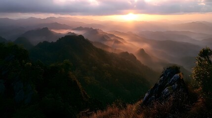 Fototapeta premium Layered mountain ranges are bathed in the warm golden glow of a dramatic sunset over a hazy landscape