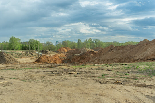 Empty construction site with piles of sand. Great background for real estate industry development promo. Sand hills at a construction site with green trees under a cloudy sky