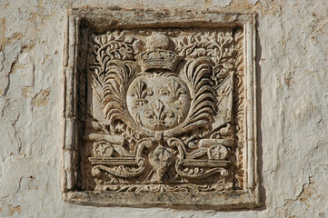 A detailed stone relief featuring a noble coat of arms with three fleurs de lis military cannons and a crown on an old plaster wall in Chora Kythira © nahhan