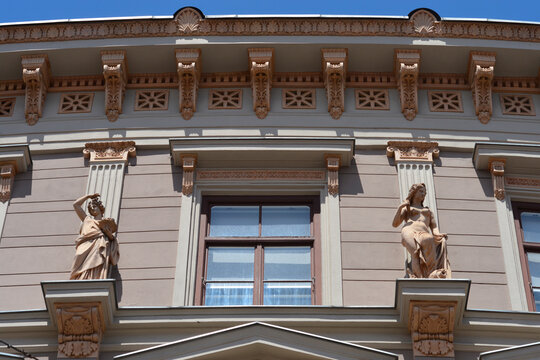A curved classic building facade features two beautiful female stone statues and detailed architectural ornaments under a clear blue sky in Zagreb, Croatia