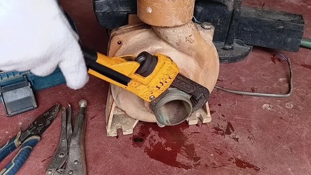 Close Up Of Technician Unscrewing And Removing A Brass Pipe Coupling From Water Pump Using A Pipe Wrench