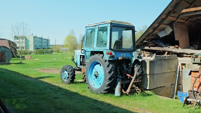 Old MTZ Belarus tractor stands near farm shed in post Soviet rural landscape