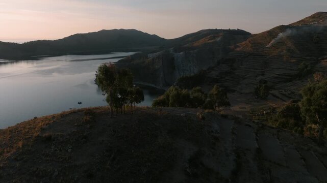 Drone view of a remote island on Lake Titicaca during sunset. Andean landscapes, traditional villages and dramatic shorelines overlook the vast lake.