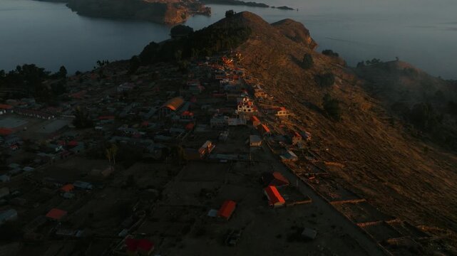 Drone view of a remote island on Lake Titicaca during sunset. Andean landscapes, traditional villages and dramatic shorelines overlook the vast lake.