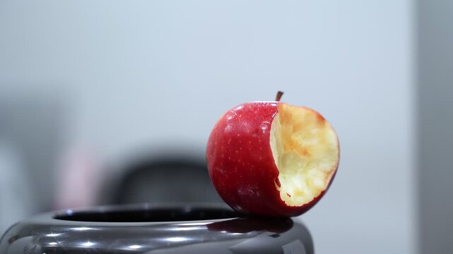 A bright red apple with a large bite rests on a glossy black surface indoors. This close-up features a shallow depth of field, highlighting the healthy snack against a blurred modern background.
