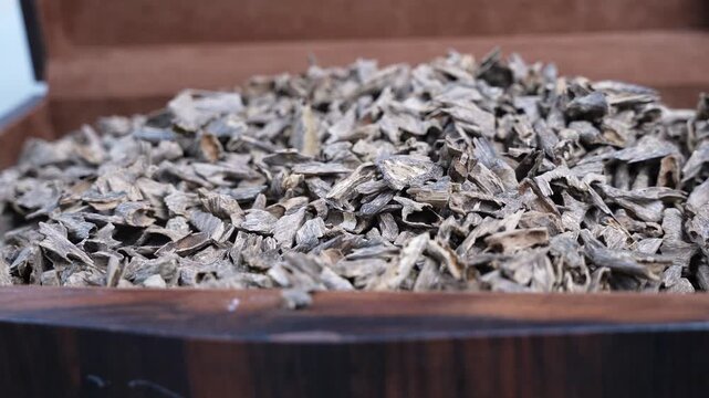 A close-up shot of premium agarwood oud chips piled inside an elegant dark wooden box. The shallow depth of field highlights the rich texture of the dry incense wood used for luxury fragrances.