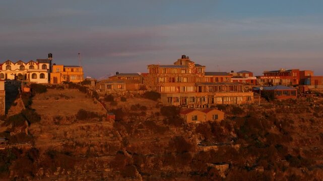 Drone view of a remote island on Lake Titicaca during sunset. Andean landscapes, traditional villages and dramatic shorelines overlook the vast lake.