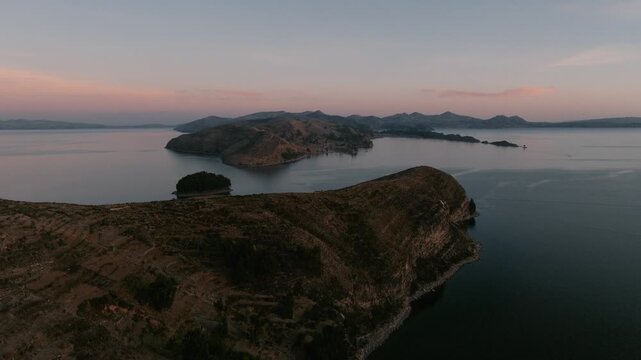 Drone view of a remote island on Lake Titicaca during sunset. Andean landscapes, traditional villages and dramatic shorelines overlook the vast lake.