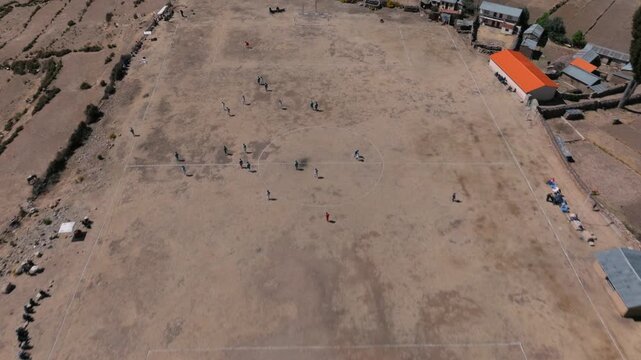 Drone view of young people playing soccer on a hillside field on Isla del Sol, with Lake Titicaca and the Bolivian Andes in the background.