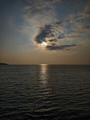 Obraz premium Dramatic sunset over the dark ocean with the sun hiding behind clouds and reflecting on the water surface.