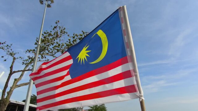 The Malaysian flag stands proudly on a sandy beach. Strong coastal winds blow the flag fiercely against the sky. This powerful display symbolizes national pride and freedom by the sea.