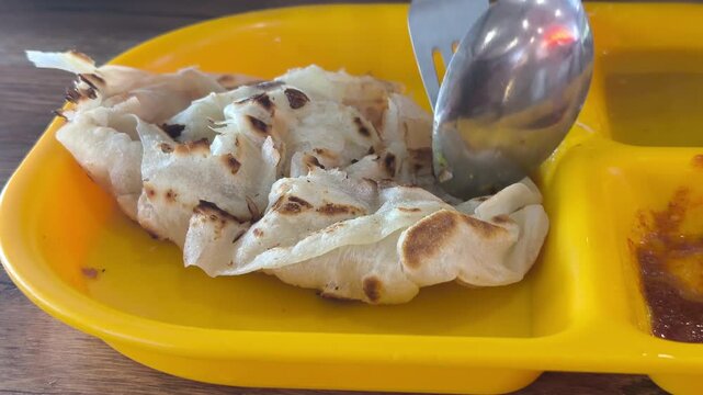 A piece of classic roti canai is served on a plate with savory dhal curry. This represents the staple, basic preparation of the dish in Malaysia. It remains immensely popular for breakfast.