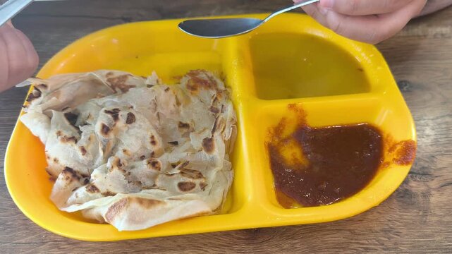A piece of classic roti canai is served on a plate with savory dhal curry. This represents the staple, basic preparation of the dish in Malaysia. It remains immensely popular for breakfast.