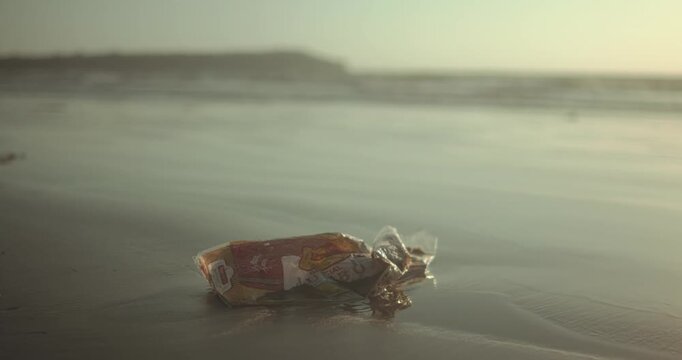 Discarded plastic bag of crumpled trash washed ashore on sandy beach, a stark symbol of ocean pollution and harm to marine habitats, urging conservation and cleanup efforts