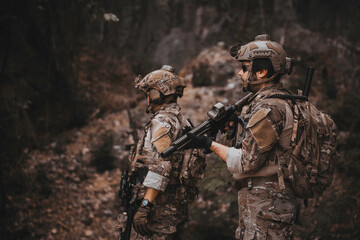 Obraz premium Two armed military operators secure an area during a tactical mission, holding rifles while patrolling a dense forest wilderness for defensive strategy, combat readiness, and national security.