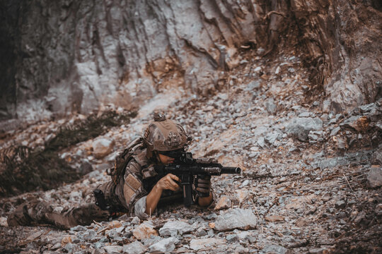Armed tactical operator aiming rifle during military combat mission in outdoor nature environment. Professional private military contractor conducting security patrol operation in forest wilderness.