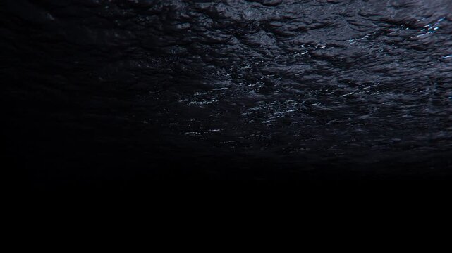 A view from the bottom looking up at the water above, the underwater world, and the glare of moonlight. Nighttime lighting on the right side of the screen.