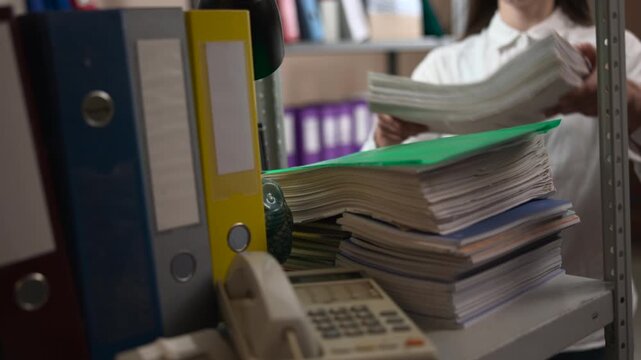 Office shelf with stacked files, binders, and telephone in the foreground