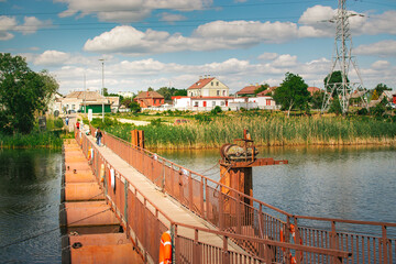 floating pontoon bridge across river with reeds and town landscape © Vasilisa Dorofeeva