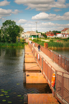 pontoon pedestrian bridge across river with ducks and water lilies on sunny day