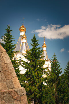 golden domes of orthodox church behind evergreen trees and stone wall