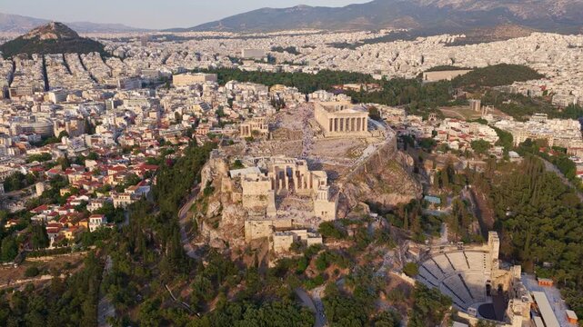 Majestic aerial view flying over the acropolis of athens, showing the parthenon, the propylaea, and the odeon of herodes atticus, with the sprawling city and mount lycabettus in the background
