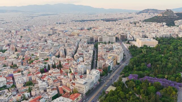Beautiful aerial view of the city of athens with the historic zappeion hall and the national garden. The acropolis and lycabettus hill are visible in the background against a hazy sky