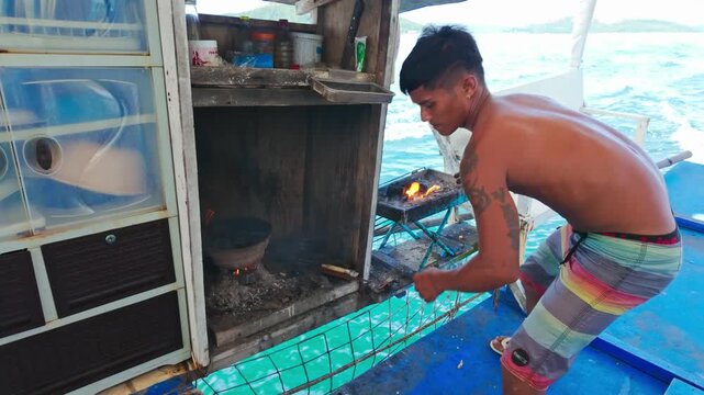 Young crew member lights charcoal stove to cook meals on Coron tour boat now