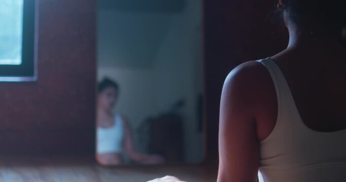 Calm moment of reflection as a woman sits quietly before a mirror following an indoor fitness and wellness session.