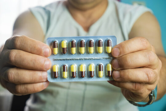 The image shows the hands of a man holding a package of medicines. Medicines are presented in the form of capsules arranged in two rows.
