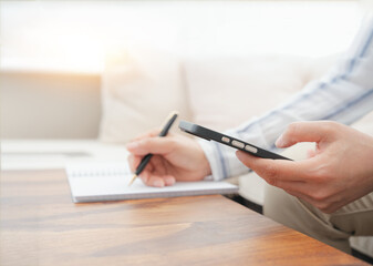 Fototapeta premium Professional reviewing CRM information on smartphone while taking notes. Email marketing, customer support, business software, workflow management, SaaS dashboard and remote work concept.