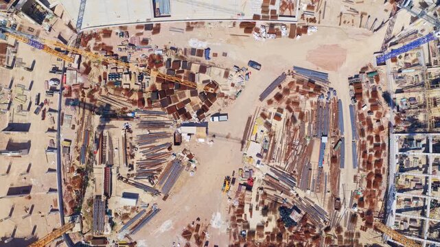 Impressive aerial top-down view showing the entire construction process of a large stadium, from the initial foundations and materials on the ground to the near-completion of the structure
