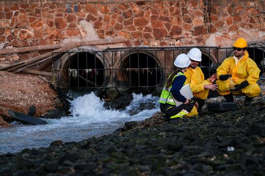 Environmental specialists in hazardous material protective gear conducting water quality sampling and field investigation near an industrial site drainage area.