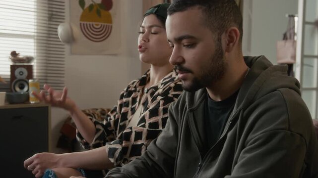 Diverse young roommates sitting on couch, checking or verifying information online on smartphone, arguing while preparing for exam or test. Suitable for education reference website, student lifestyle