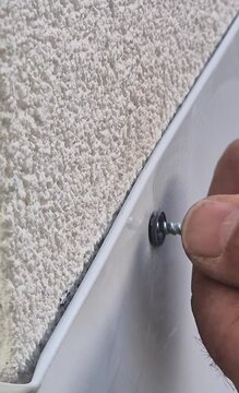 Vertical close up video of inserting a screw into a metal roof flashing after drilling, 9:16 aspect ratio