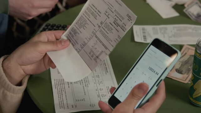Hands of young male housemates holding smartphone with calculator app while reviewing past due utility bills and invoices. Video suits financial literacy, student debt, and budgeting promotions