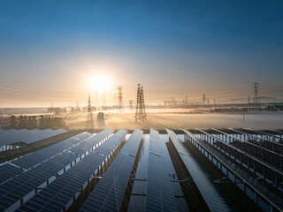 Obraz premium Solar power station with transmission towers at sunrise over misty fields