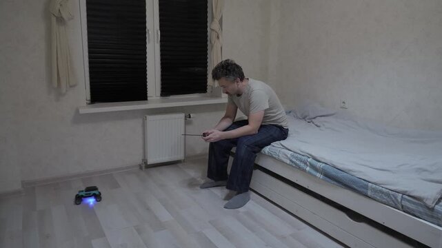 Man playing RC car alone at night. Individual resting in simple dwelling engaged with electronic devices during late hours