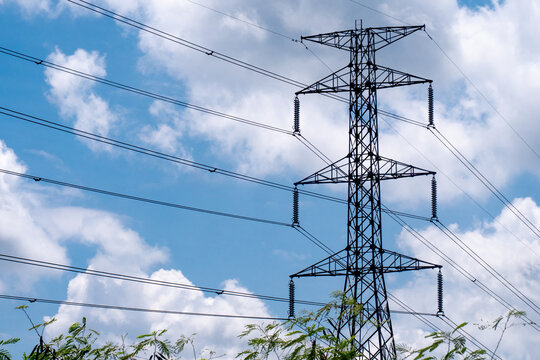 ** Tall Electrical Transmission Tower Against a Blue Sky with White Clouds and Green Foliage in the Foreground

**