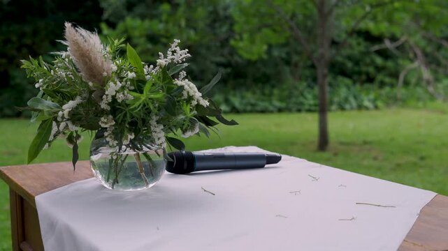 Micr&oacute;fono y florero sobre un altar de ceremonia al aire libre en el campo durante un d&iacute;a soleado, casamiento, celebraci&oacute;n, romance, evento social y boda campestre