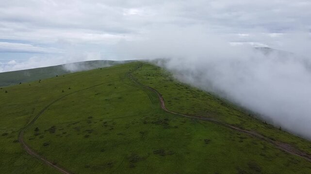 Drone flying through low clouds over green mountains