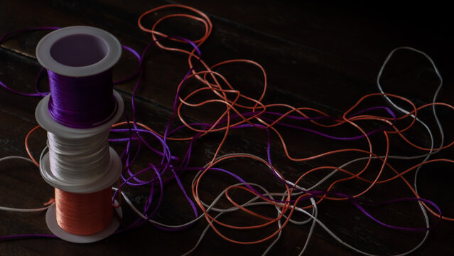 Stack of colorful thread spools with tangled string on dark wooden background